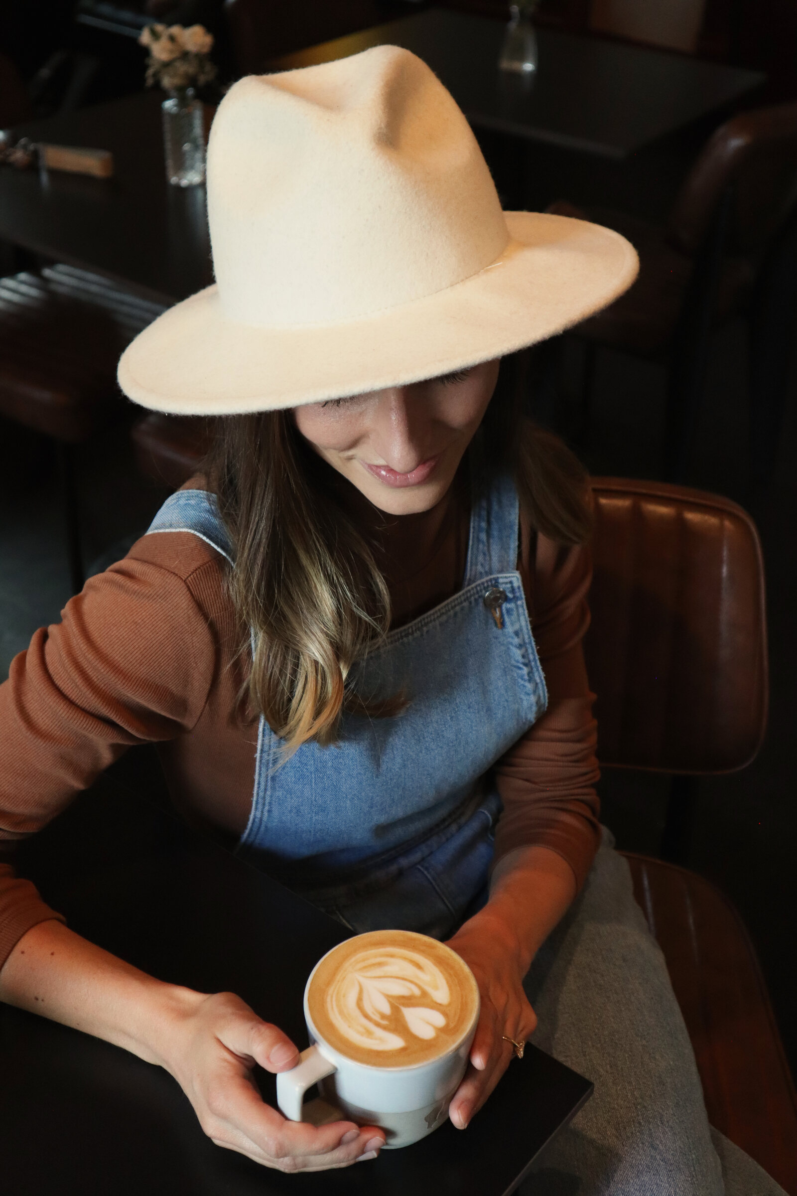 A woman in a wide-brim hat holding a latte