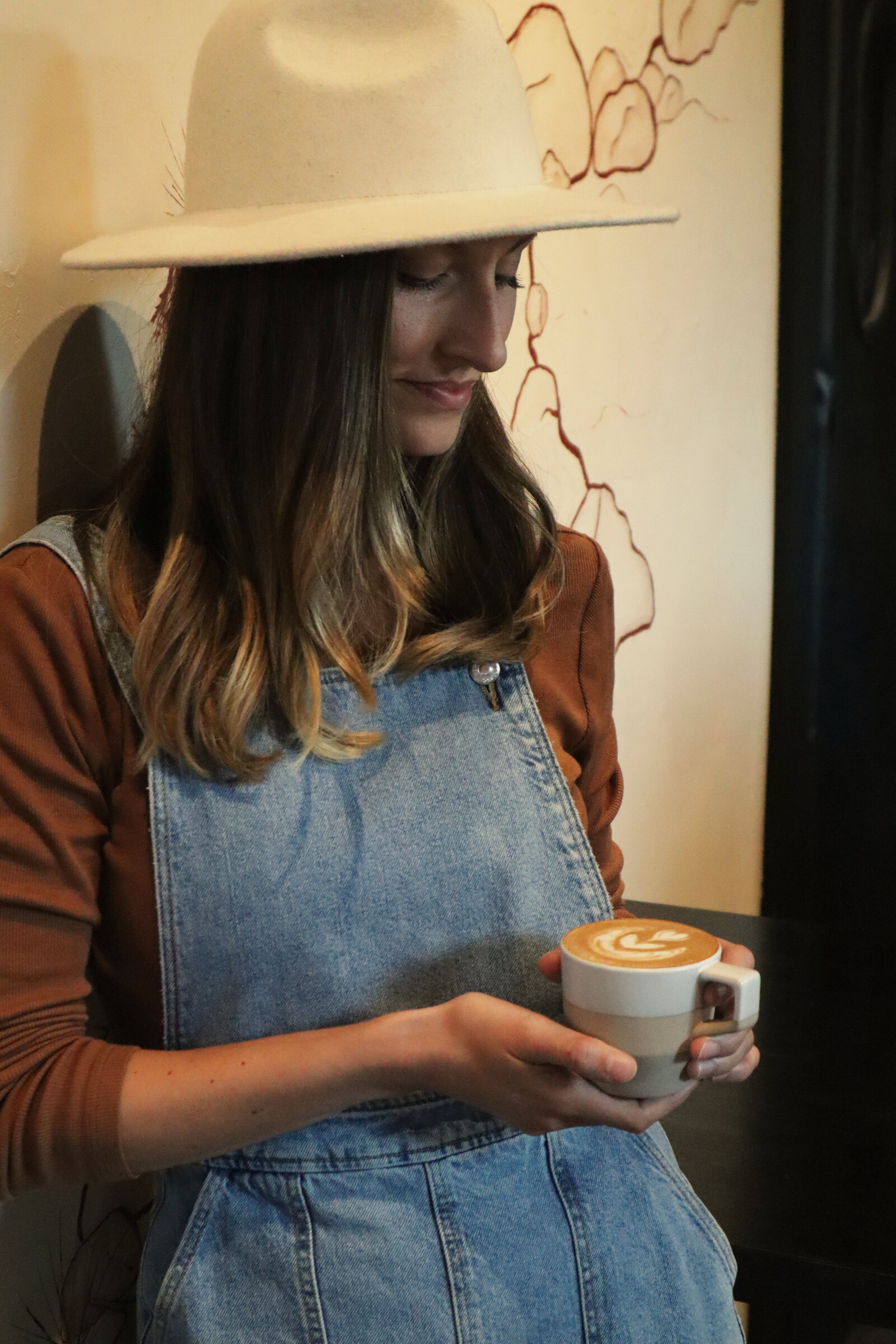 A woman in overalls holding a latte