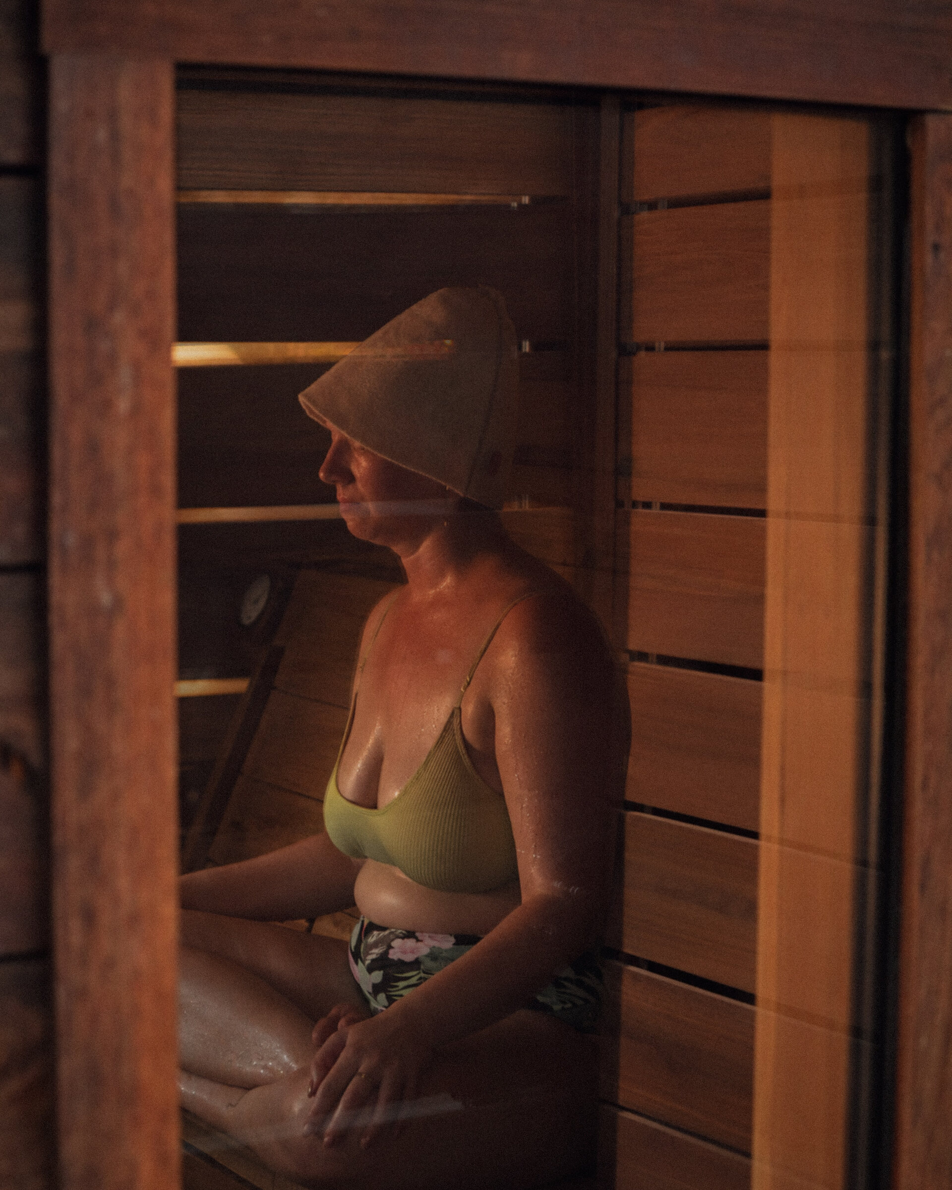 A woman resting in a cedar sauna, seen through the window