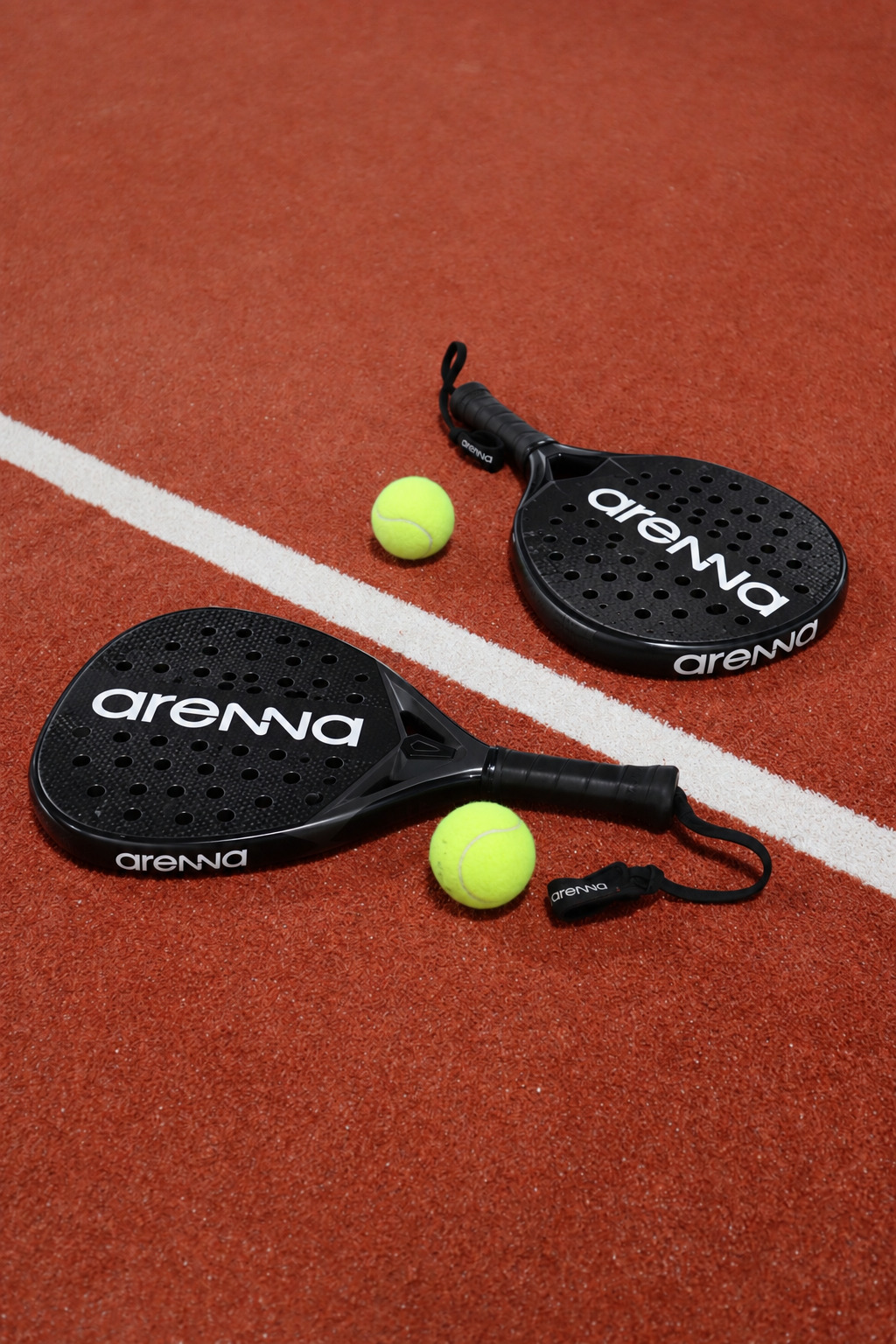 Two padel rackets and balls on a terracotta court