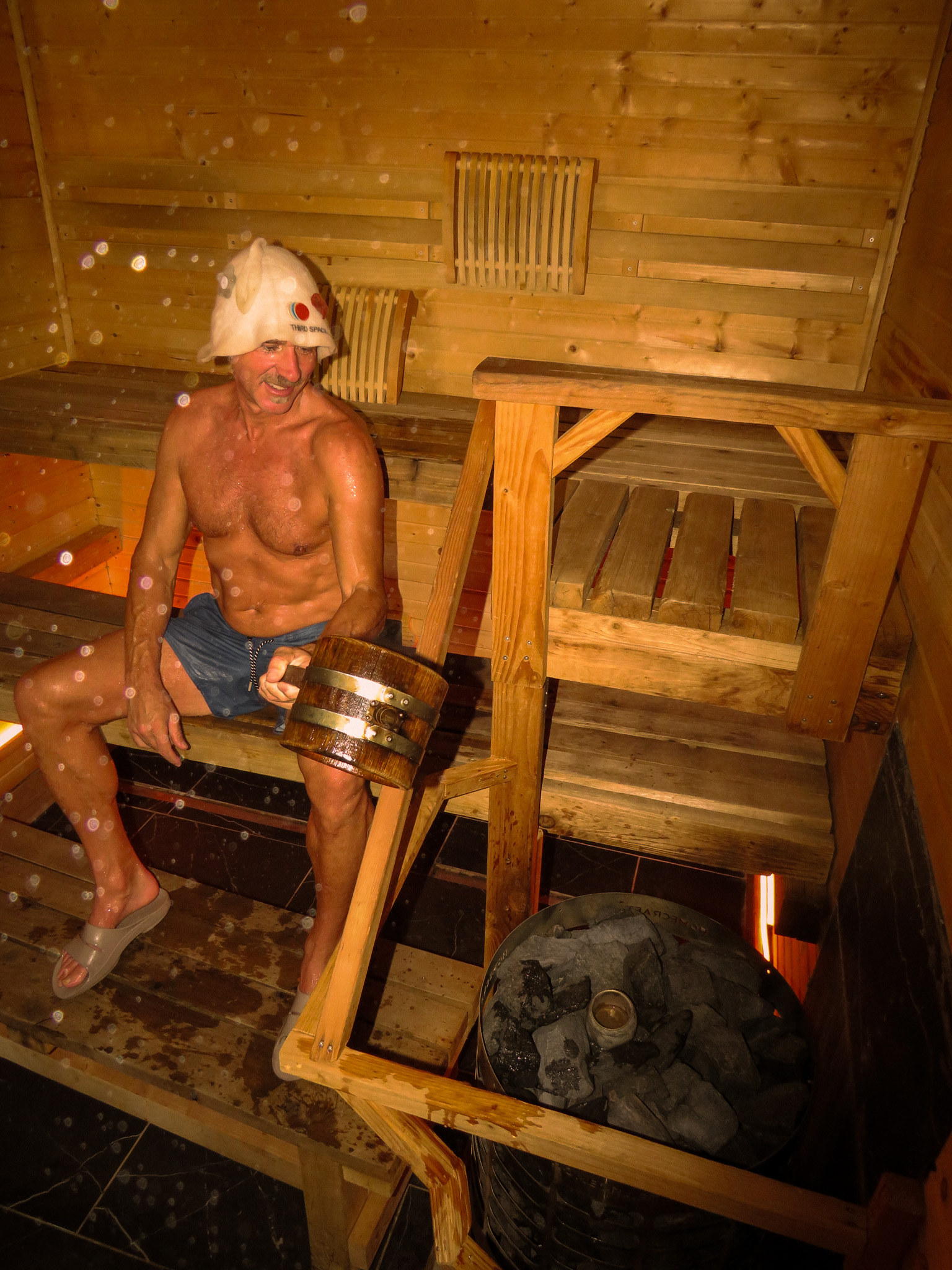 A regular with a wooden bucket in the sauna, steam drifting