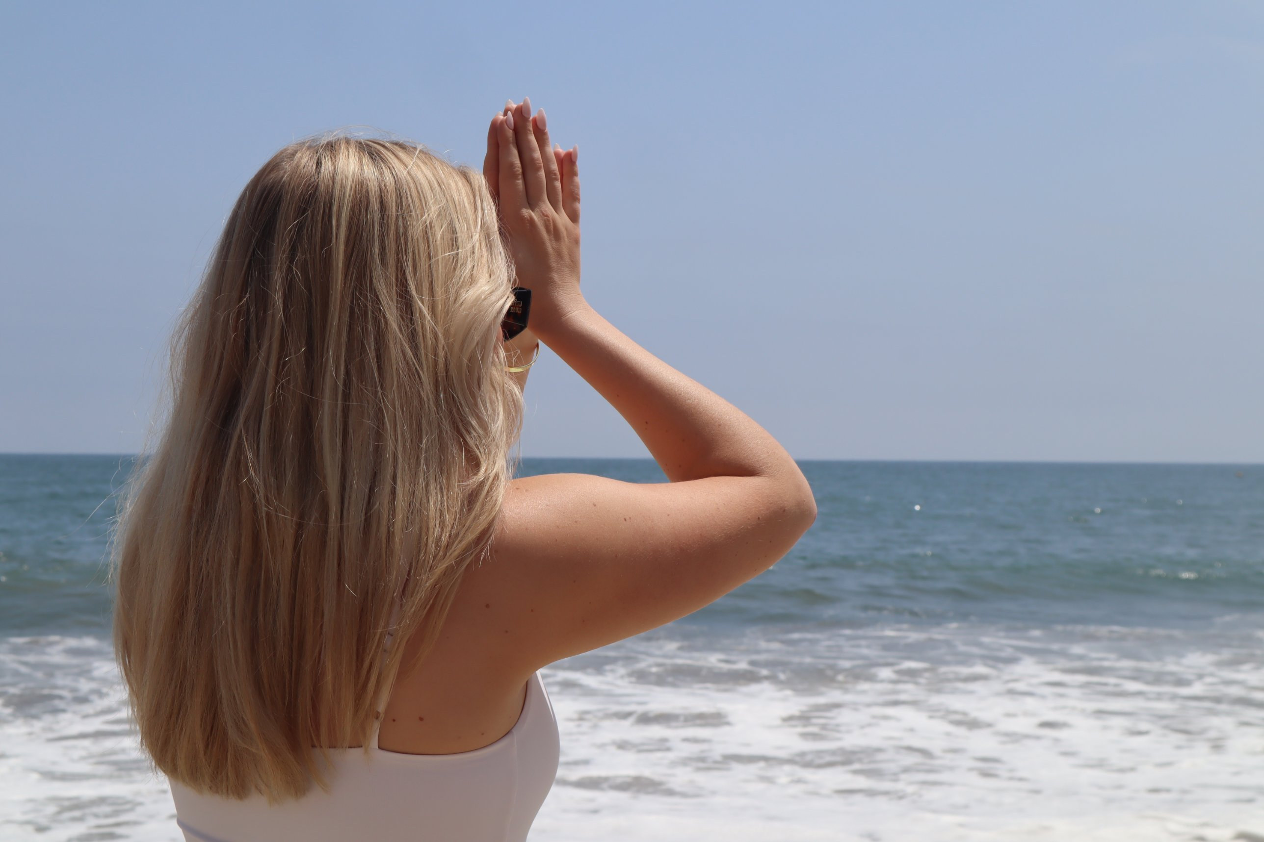 A woman with hands raised in prayer facing the ocean